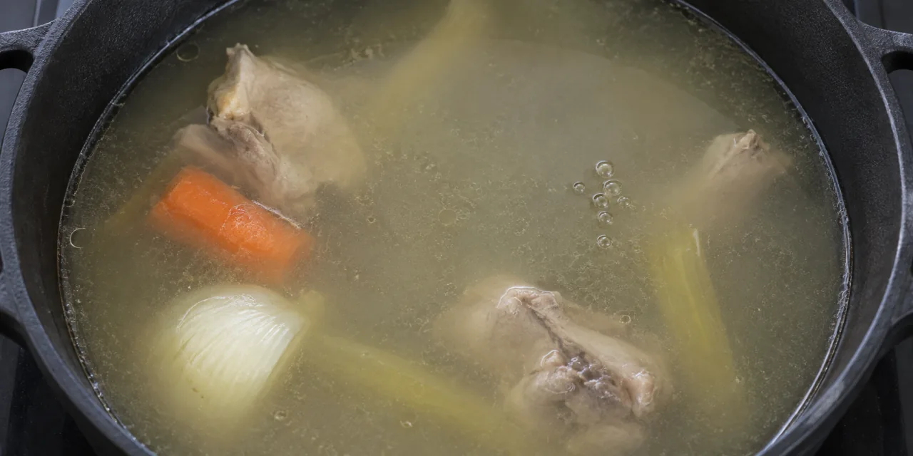 Bouillon clair au frémissement dans une cocotte noire, quelques bulles isolées à la surface, volaille et légumes immergés